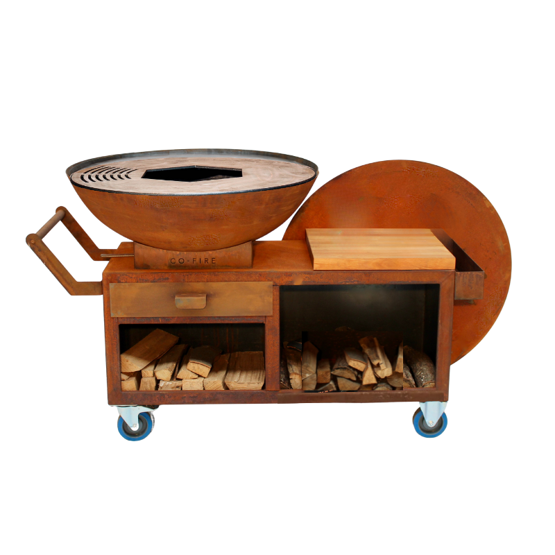Afbeelding van de Co-fire GrillRing PRO Set: een grote professionele grillring barbecue met vuurschaal, stevig onderstel en werkblad, gebruikt tijdens een buitenkookevent met meerdere gasten.